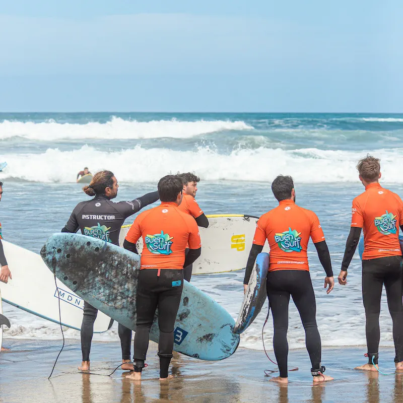 A group in Buen Surf jerseys on the sand with their boards, listening to the instructor before going in